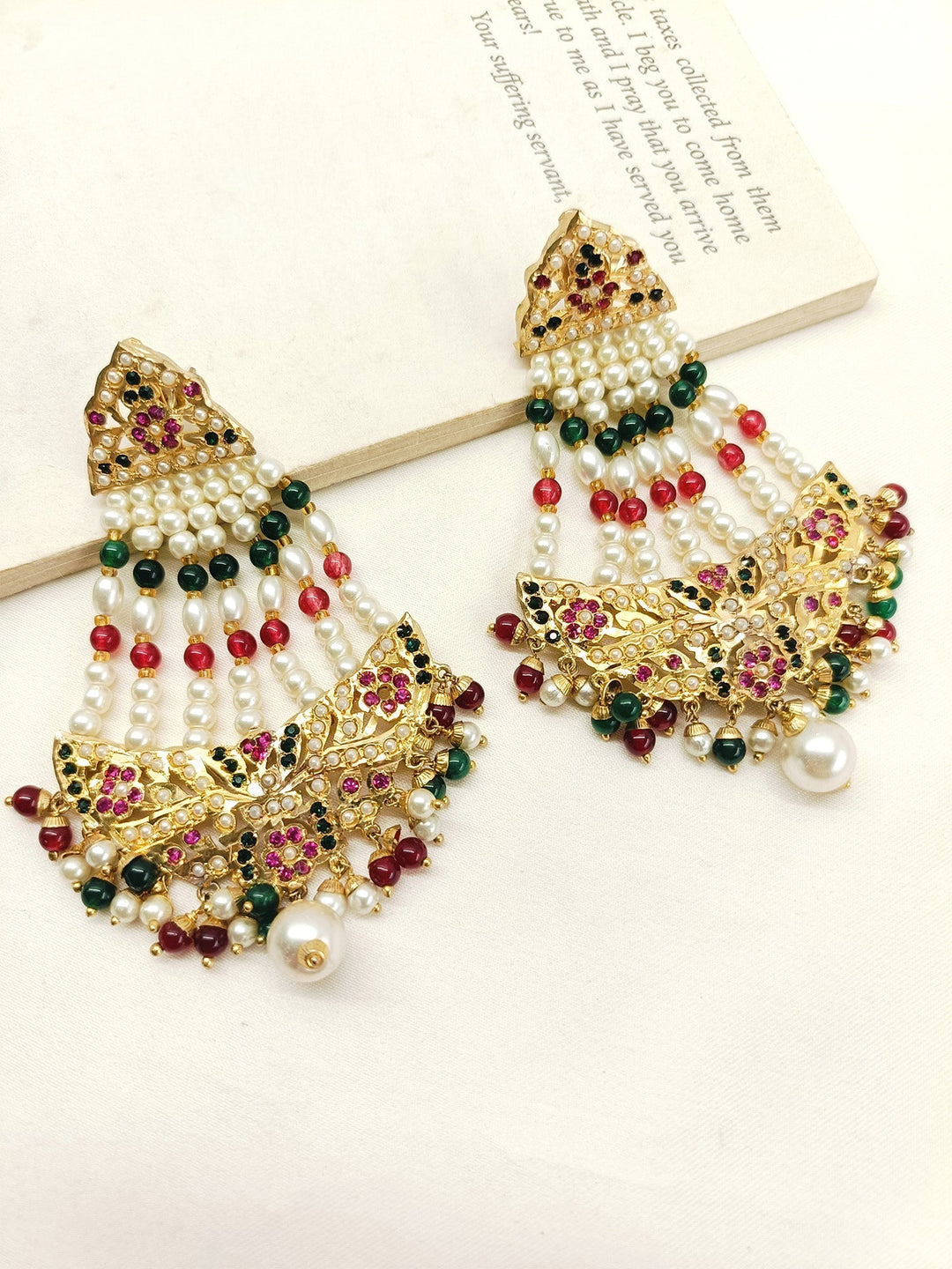 Traditional long jadau earrings with intricate gold texture work and ruby and green bead accents with small bead hangings 