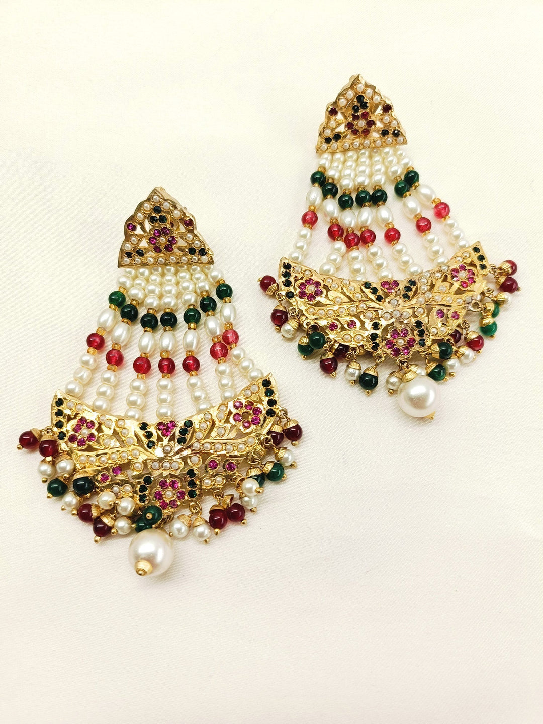  Exquisite jadau earrings adorned with gold texture work, ruby and green stones, and delicate bead hangings