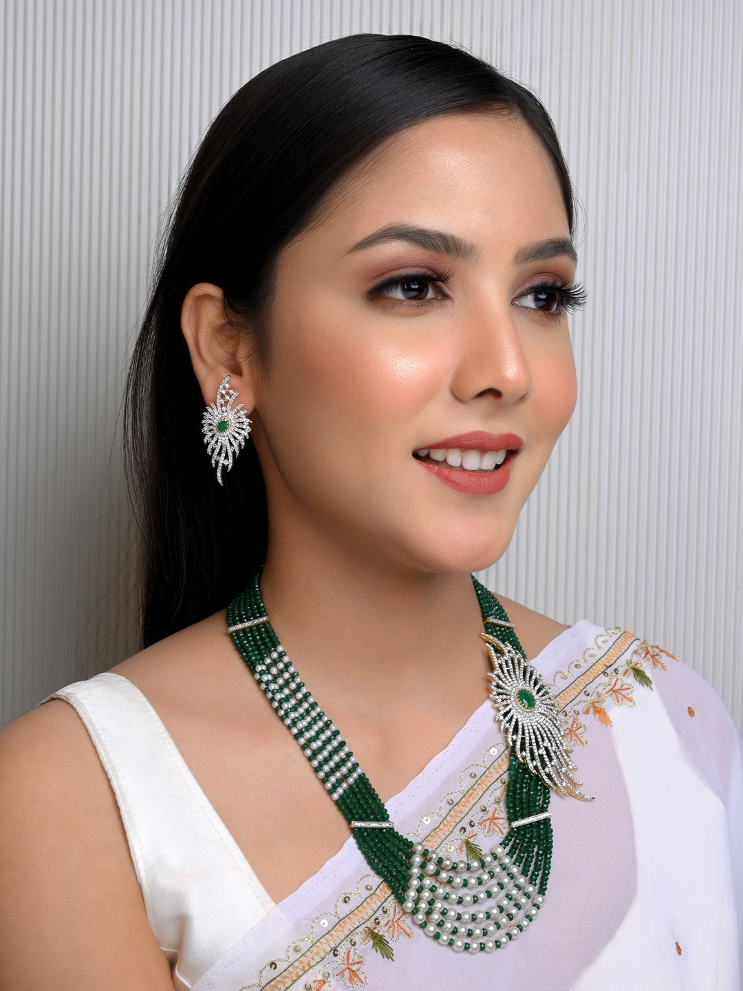 This elegant Himangi Emerald American Diamond Necklace Set features multiple layered beads and a stunning gold plated brass metal chain with a side broach, perfect for special occasions