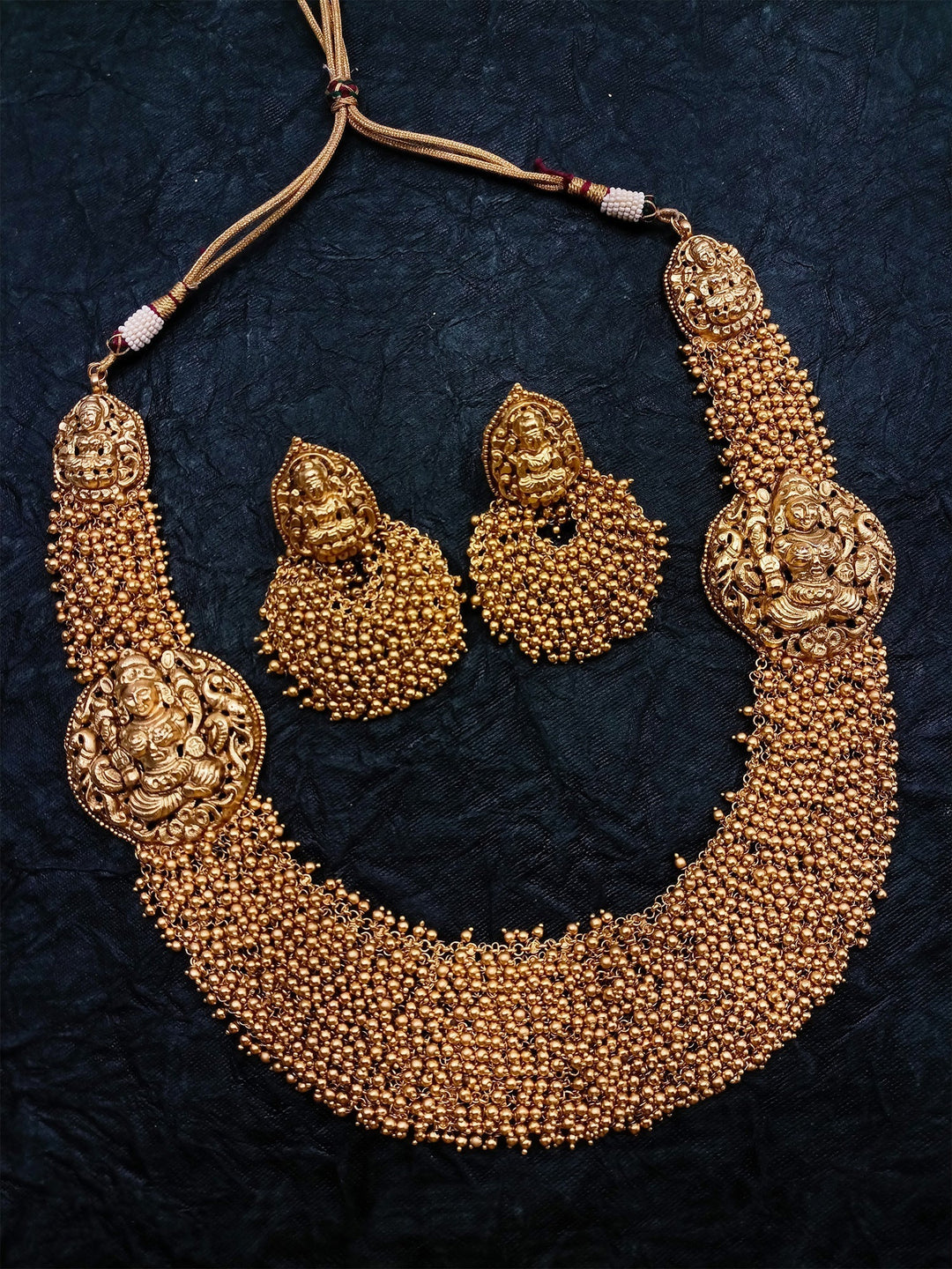 Long gold necklace set with intricate temple design and red beads